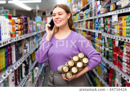 woman buys canned beer in hypermarket and talking on mobile phone 84716426