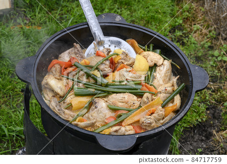 Cast iron pot with boiling soup of chicken, tomatoes, onions and peppers outdoors on the grass Cast iron pot with boiling soup of chicken, tomatoes, onions and peppers outdoors on the grass 84717759