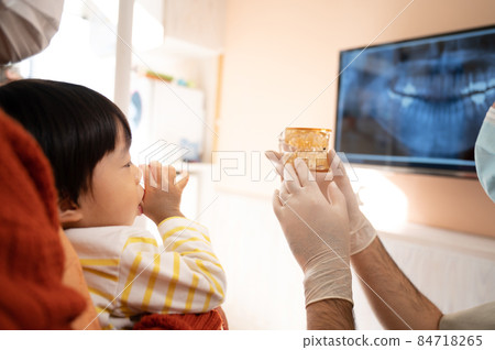 Image of a pediatric dentist explaining a child's teeth to a mother using a model 84718265