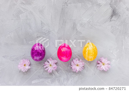 Colorful eggs and spring pink sakura cherry blossom flowers on gray background. Easter celebration concept. Top view, flat lay, copy space Colorful eggs and spring pink sakura cherry blossom flowers on gray background. Easter celebration concept. Top view, flat lay, copy space 84720271