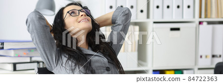 Happy contented woman resting in office sits with laptop and holds hands behind head closeup Happy contented woman resting in office sits with laptop and holds hands behind head closeup 84722363