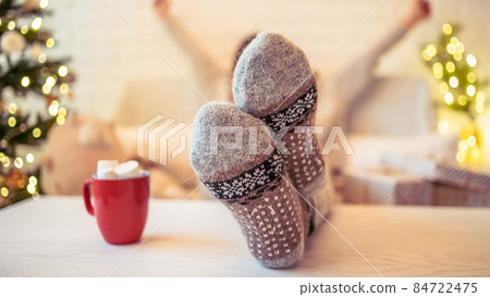 Unfocused, blur woman sitting and relaxation near christmas tree with cup of cocoa and marshmallows after finishing pakking gift boxes for family. Unfocused, blur woman sitting and relaxation near christmas tree with cup of cocoa and marshmallows after finishing pakking gift boxes for family. 84722475