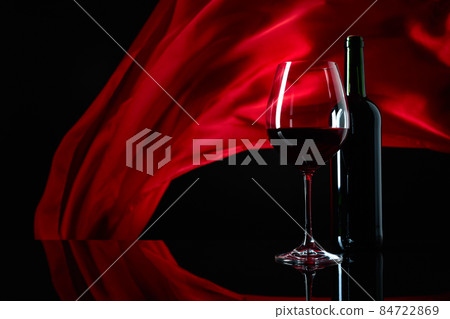 Wineglass and bottle of red wine on a black reflective background. 84722869