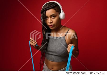 Determined African sportswoman in gray sportswear exercising with an elastic fitness strap during routine workout, isolated over red background with copy space. Body positivity, fitness, sport concept 84725732
