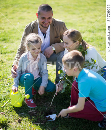 Parents with children plant a tree in the park in spring Parents with children plant a tree in the park in spring 84726063