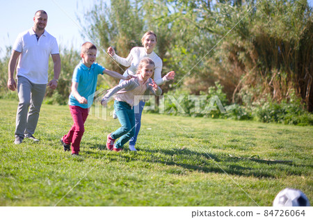 Father with mother with two children enjoy playing soccer on lawn in summer park Father with mother with two children enjoy playing soccer on lawn in summer park 84726064