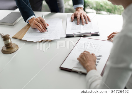 law concept The barrister standing, holding a pen in his hand, and reading the point that seems to be obscure for him to his helper who sits opposite to him 84726492