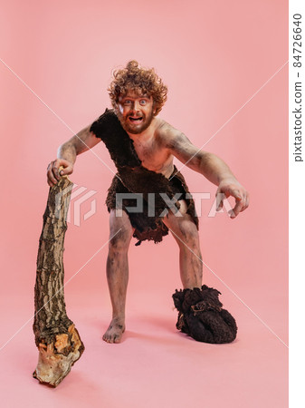 Full-length portrait of cheerful man in character of neanderthal, primitive person isolated over pink background 84726640