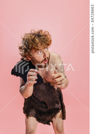 Cropped portrait of man in character of neanderthal wearing animal skin cloth standing in fear isolated over pink background 84726663