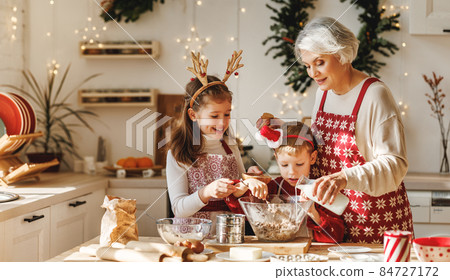 Two little kids making Christmas homemade cookies together with elderly grandmother in kitchen 84727172