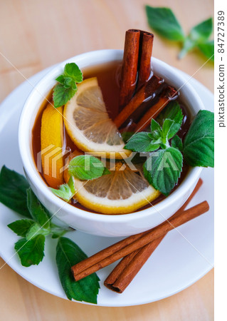 Black and green tea with lemon, cinnamon sticks and mint leaves. Hot drink. Healthy melissa tea natural organic aromatic drink in cup. Summer, Autumn winter warming drink. 84727389