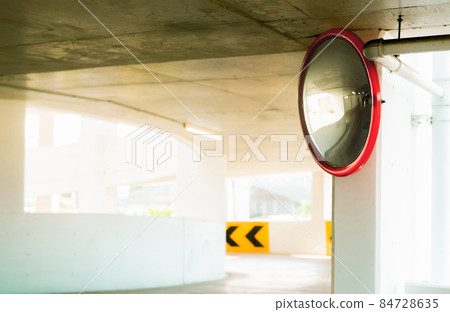 Convex safety mirror at curve of indoor car parking lot to reduce risk of accidents from blind corner or blind spots. Convex circular safety mirror in multi-level parking garage. Indoor traffic convex 84728635