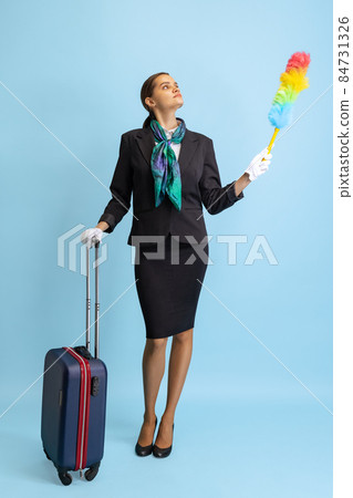 Studio shot of beautiful young girl, flight attendant in uniform with suitcase isolated on blue studio background. Studio shot of beautiful young girl, flight attendant in uniform with suitcase isolated on blue studio background. 84731326