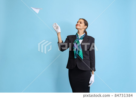 Half-length portrait of beautiful young girl, flight attendant in black uniform posing isolated on blue studio background. Half-length portrait of beautiful young girl, flight attendant in black uniform posing isolated on blue studio background. 84731384