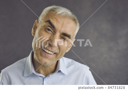 Close up portrait of happy senior man winking happily at camera giving sign that has good offer. Funny caucasian man with gray hair dressed in shirt stands on gray background. Banner. Close up portrait of happy senior man winking happily at camera giving sign that has good offer. Funny caucasian man with gray hair dressed in shirt stands on gray background. Banner. 84731828