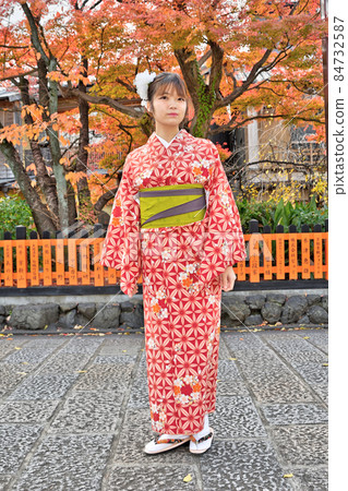 A woman in kimono standing with autumn leaves on her back A woman in kimono standing with autumn leaves on her back 84732587