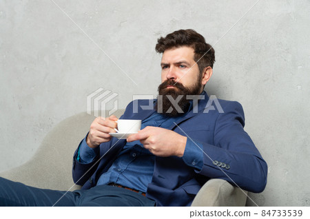 Bearded man relax drinking tea or coffee in rest armchair during work break, relaxing Bearded man relax drinking tea or coffee in rest armchair during work break, relaxing 84733539