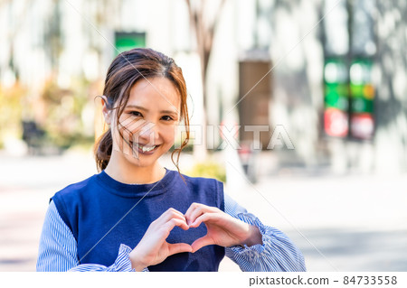 A woman who makes a cute heart mark outdoors 84733558