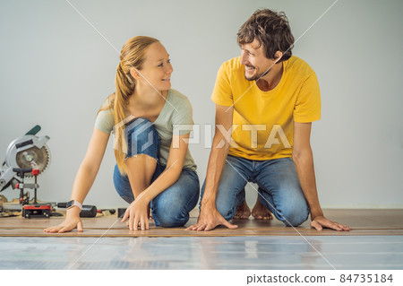 Married couple installing new wooden laminate flooring on a warm film floor. Infrared floor heating system under laminate floor 84735184