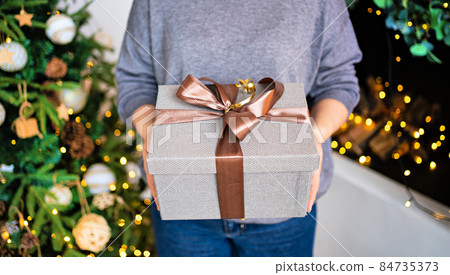 hands with gray gift box with brown ribbon near the christmas tree 84735373