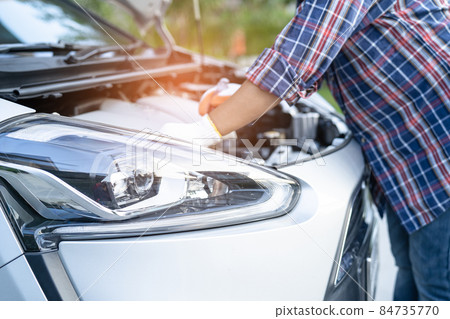 Asian auto mechanic check for repair under the hood of broken down car on the side of the road. 84735770
