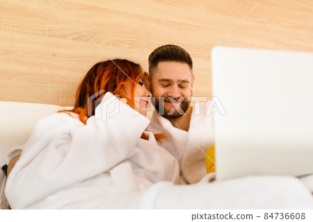 Happy young couple in bathrobes lie in bed Happy young couple in bathrobes lie in bed 84736608
