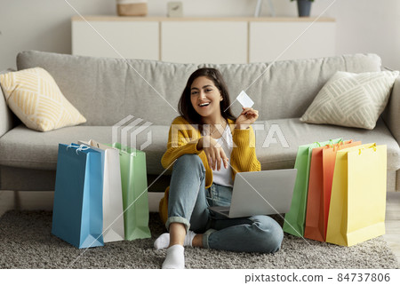 Excited arab woman feeling happy over big sale, using laptop and showing credit card, sitting on floor with gift bags Excited arab woman feeling happy over big sale, using laptop and showing credit card, sitting on floor with gift bags 84737806