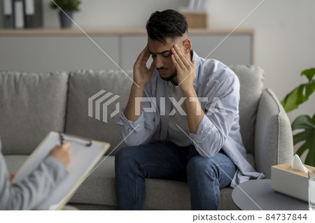 Desperate arab guy suffering from nevrous breakdown, having session at psychologist's office, touching temples Desperate arab guy suffering from nevrous breakdown, having session at psychologist's office, touching temples 84737844
