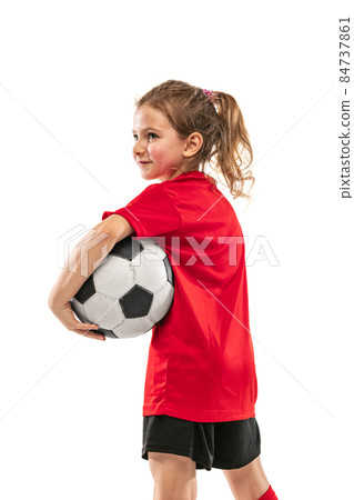 Cropped side view portrait of girl, child, in red football player uniform posing with ball isolated over white background 84737861