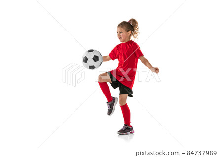 Full-length portrait of girl, child, football player in red uniform training, kicking ball with knee isolated over white background Full-length portrait of girl, child, football player in red uniform training, kicking ball with knee isolated over white background 84737989