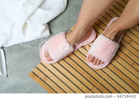 Female legs in pink slippers on bamboo on gray textured floor 84738410