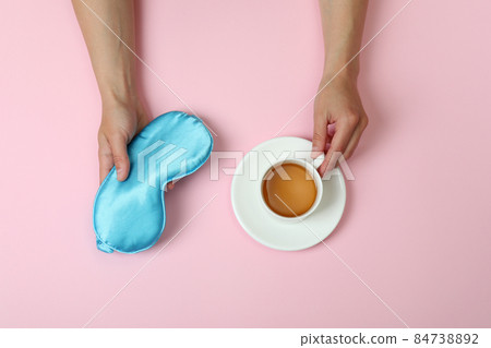 Female hands hold sleep mask and tea on pink background Female hands hold sleep mask and tea on pink background 84738892