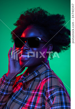 Close-up African young girl's portrait on dark green studio background in purple neon light. Afro hairdo. Concept of human emotions Close-up African young girl's portrait on dark green studio background in purple neon light. Afro hairdo. Concept of human emotions 84740347