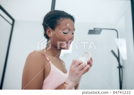 A cute young woman holding a jar of face cream in hands 84741222