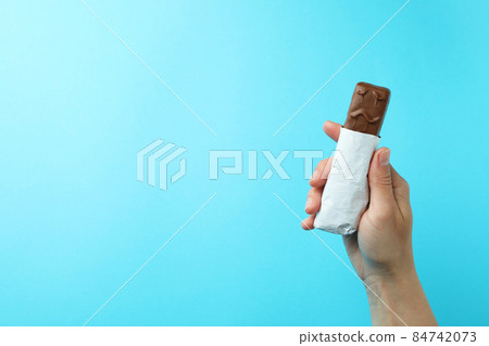 Female hand holds tasty candy bar on blue background Female hand holds tasty candy bar on blue background 84742073