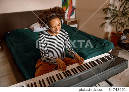 Joyful female musician playing synthesizer at home Joyful female musician playing synthesizer at home 84742661
