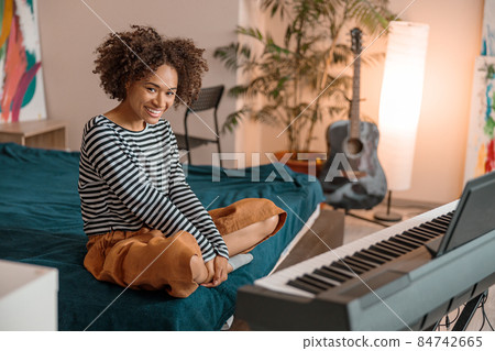 Joyful female musician sitting near synthesizer at home Joyful female musician sitting near synthesizer at home 84742665