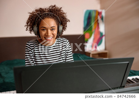 Joyful multiracial woman playing synthesizer at home Joyful multiracial woman playing synthesizer at home 84742666
