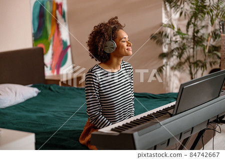 Smiling young woman sitting near synthesizer at home Smiling young woman sitting near synthesizer at home 84742667