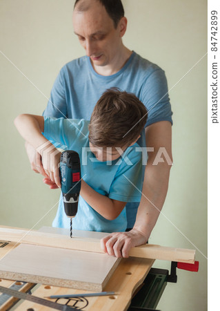 Dad and son work together while standing at workbench Dad and son work together while standing at workbench 84742899