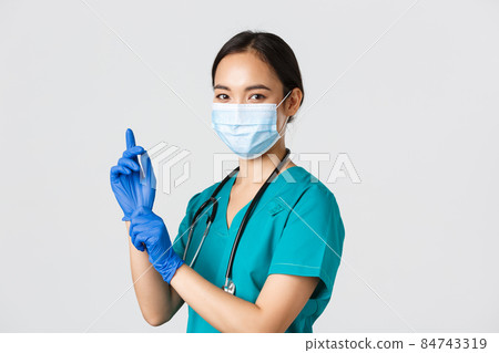 Covid-19, coronavirus disease, healthcare workers concept. Professional confident asian female doctor, nurse in medical mask and scrubs, put on rubber gloves for examination, white background Covid-19, coronavirus disease, healthcare workers concept. Professional confident asian female doctor, nurse in medical mask and scrubs, put on rubber gloves for examination, white background 84743319