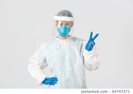 Covid-19, coronavirus disease, healthcare workers concept. Sassy asian female doctor, physician or tech lab in personal protective equipment showing peace sign, standing white background Covid-19, coronavirus disease, healthcare workers concept. Sassy asian female doctor, physician or tech lab in personal protective equipment showing peace sign, standing white background 84743371