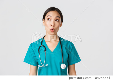 Healthcare workers, preventing virus, quarantine campaign concept. Impressed and amazed asian female doctor, nurse in medical scrubs looking upper left corner pleased, white background 84743531