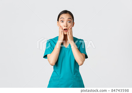 Covid-19, healthcare workers, pandemic concept. Surprised and startled asian nurse, doctor in scrubs stare at camera speechless, gasping amazed, listen to announcement, being impressed 84743598