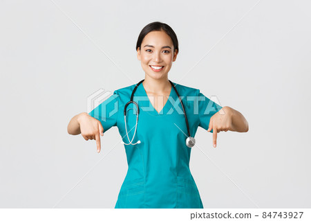 Covid-19, healthcare workers, pandemic concept. Smiling pleasant asian female doctor, therapist or physician in scrubs with stethoscope, pointing fingers down, show clinic banner Covid-19, healthcare workers, pandemic concept. Smiling pleasant asian female doctor, therapist or physician in scrubs with stethoscope, pointing fingers down, show clinic banner 84743927
