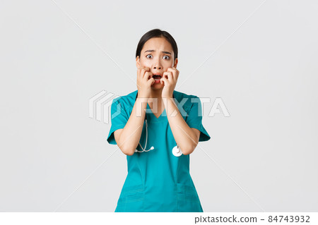 Covid-19, healthcare workers and preventing virus concept. Scared insecure asian female doctor, nurse in scrubs starts to panic from fear, biting fingernails and looking horrified, white background 84743932