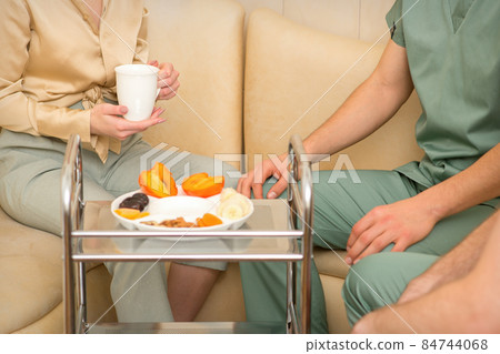 Young caucasian woman consulting with two masseurs during tea with dried fruit in the massage spa. 84744068