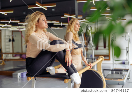 Focused young woman resting after stretching and practicing some gymnastic moves in studio with her friend 84744117