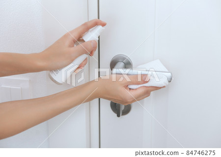 Cleaning black door handles with an antiseptic white wet wipe. Sanitize surfaces prevention in hospital and public spaces against corona virus. Woman hand using towel for cleaning. 84746275