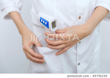 Temperature measurement gun in doctor hands. Close-up shot of doctor wearing protective surgical mask ready to use infrared isometric thermometer gun to check body temperature for virus symptoms. Temperature measurement gun in doctor hands. Close-up shot of doctor wearing protective surgical mask ready to use infrared isometric thermometer gun to check body temperature for virus symptoms. 84746284